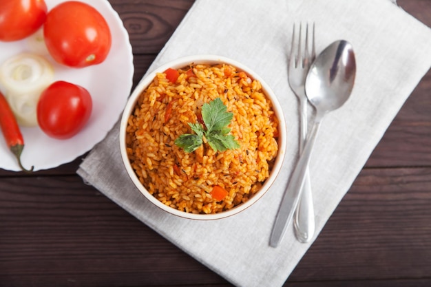 Рисовые помидоры Jollof и острый перец на синей тарелке вилка ложка на льняной салфетке на коричневом деревянном фоне Национальная кухня Африки