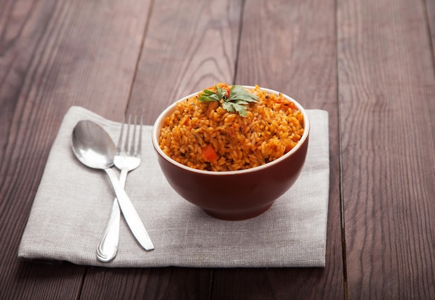 Рисовые помидоры Jollof и острый перец на синей тарелке вилка ложка на льняной салфетке на коричневом деревянном фоне Национальная кухня Африки