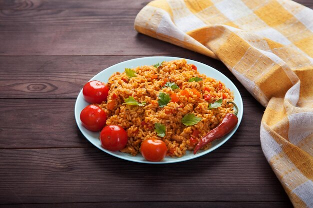 Рис Jollof, помидоры и острый перец на синей тарелке, льняная салфетка на коричневом деревянном фоне. Национальная кухня Африки.