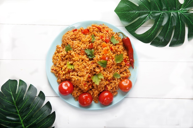 Jollofrijst met tomaten en hete pepers op een blauw bord op een wit bord met monsterapalmbladeren nationale keuken van afrika