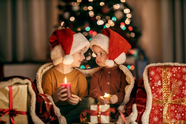 クリスマスと新年の夜に手にキャンドルを持って家に座っているジョリーの兄弟と姉妹