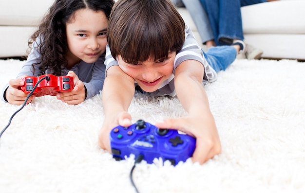 Photo jolly children playing video games lying on the floor