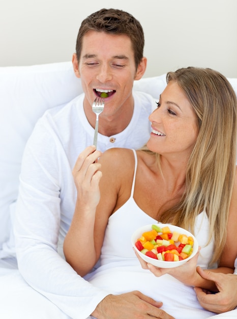 Jolly couple eating fruit lying on their bed 