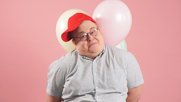 Jolly fat man in a red baseball cap holding balloons on a pink background