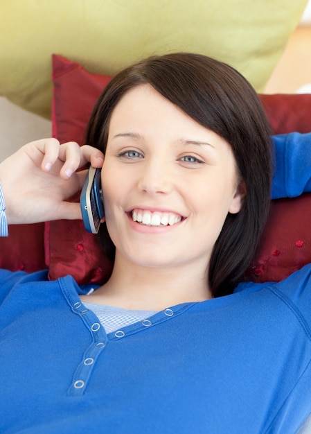Photo jolly teen girl talking on phone lying on a sofa