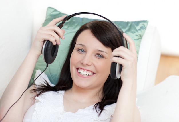 Photo jolly woman putting headphones lying on a sofa