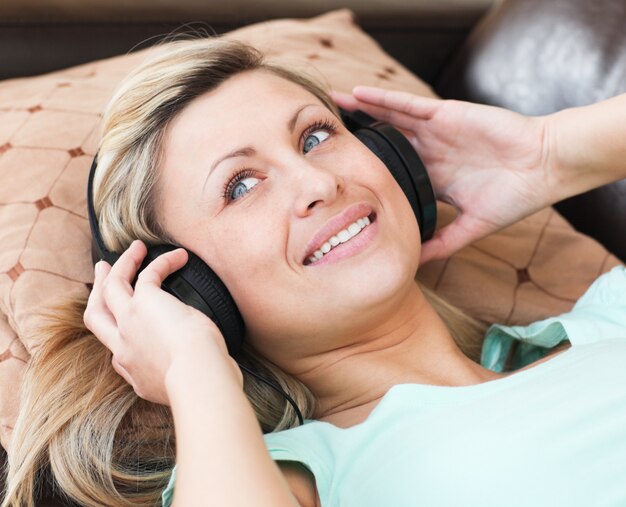 Jolly woman with headphones on lying on a sofa