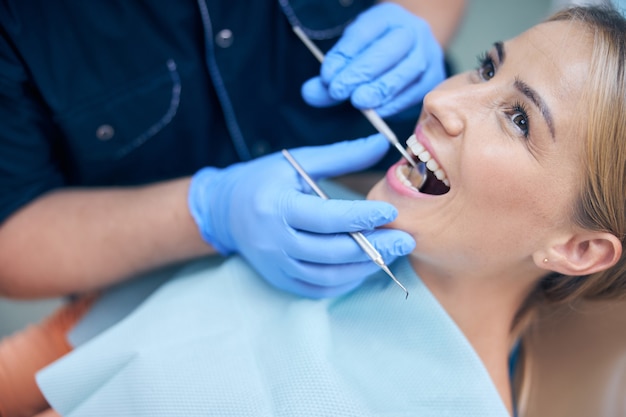 Photo jolly young woman being examined by dentist