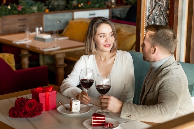 Jong aanhankelijk paar praten door dessert en glas rode wijn zittend door tafel geserveerd na een romantische lunch in restaurant