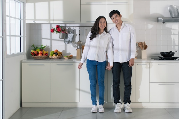 Jong aantrekkelijk Aziatisch paar dat wit overhemd en jeans in witte keuken draagt.
