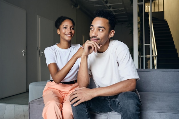 Jong aantrekkelijk casual Afro-Amerikaans koppel dromerig zittend op de bank samen in een modern huis