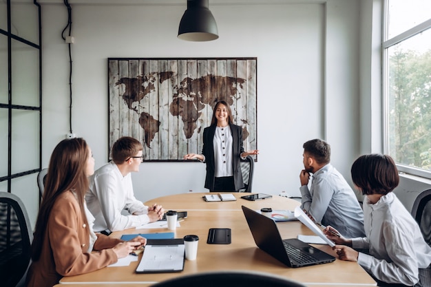 Jong aantrekkelijk meisje dat voor haar collega's rapporteert. Werkvergadering op kantoor