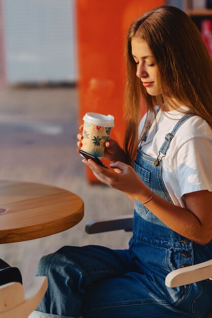 Jong aantrekkelijk mooi meisje bij koffie met koffie en telefoon bij ochtendstralen