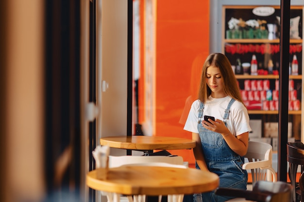 Jong aantrekkelijk mooi meisje bij koffie met koffie en telefoon bij ochtendstralen