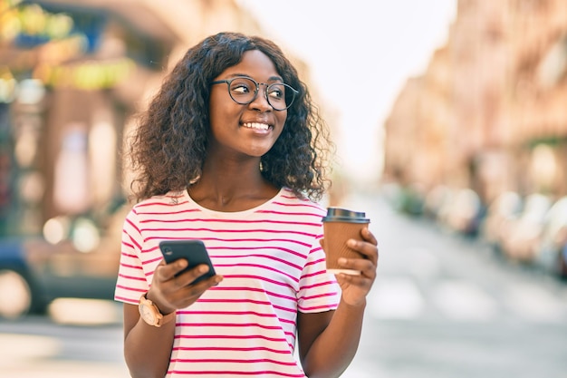 Jong Afrikaans Amerikaans meisje met behulp van smartphone koffie drinken in de stad