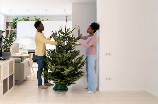 Jong afrikaans stel dat een levende kerstboom ophangt en samen thuis voorbereidt op de wintervakantie