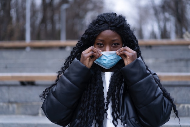 Jong afro-meisje met medisch gezichtsmasker in een Afrikaans meisje in de buitenlucht dat gezichtsmasker gebruikt