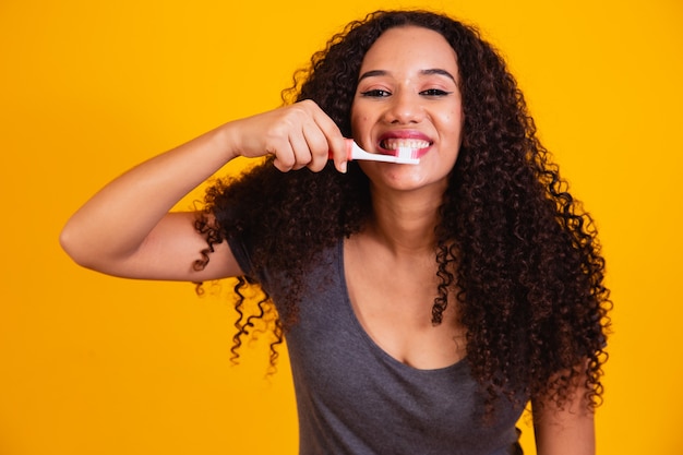 Jong afro meisje tandenpoetsen op gele achtergrond. Afro vrouw haar tanden poetsen. Mondgezondheidsconcept