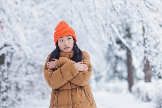 Jong Aziatisch meisje bevriest in het park, wachtend op een date op een besneeuwde winterdag, een warm aangeklede vrouw