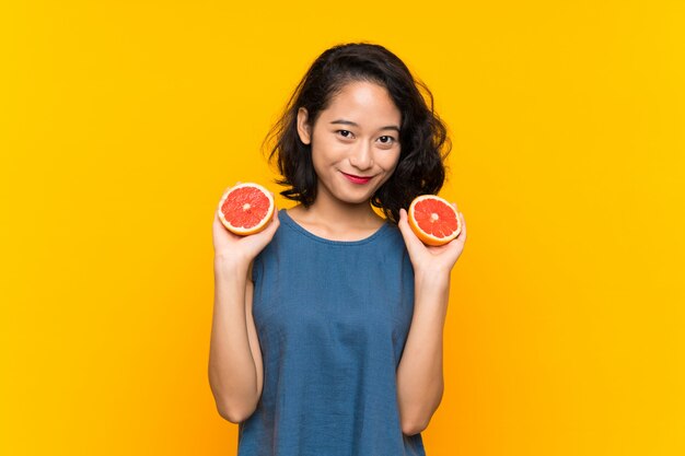 Jong Aziatisch meisje dat een grapefruit over geïsoleerde oranje achtergrond houdt