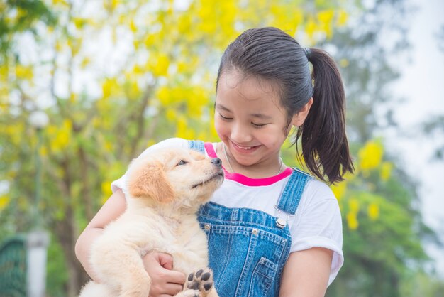 Jong Aziatisch meisje dat een kleine golden retrieverhond in park houdt