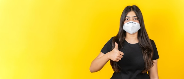 Jong Aziatisch meisje dat een medisch gezichtsmasker in vrijetijdskleding draagt die op gele achtergrond wordt geïsoleerd