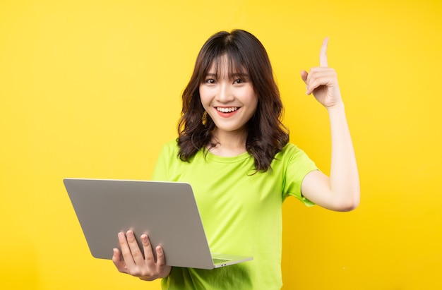 Jong Aziatisch meisje dat laptop op gele muur met behulp van
