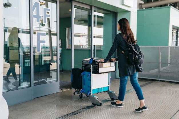 jong Aziatisch meisje met bagage die de internationale luchthaven van kansai binnenkomt. elegante vrouw rolt lichte kar met bagage door de automatische deur in vier verdiepingen. mooie dame die naar het buitenland gaat om met een rugzak te reizen.