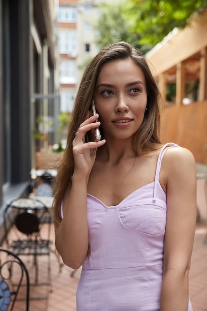 Jong Aziatisch mooi meisje in roze jurk die buiten staat te bellen met een smartphone