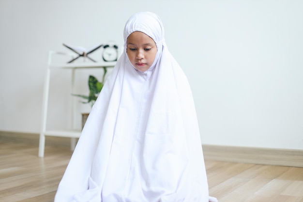 Jong Aziatisch moslimmeisje dat op een gebedsmat bidt en een van de salatprocedures uitvoert