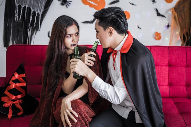 Jong aziatisch stel in kostuumheks en dracula met halloween-feest vieren en samen bier drinken op halloween-festival in de kamer thuis. concept paar vieren halloween samen thuis.