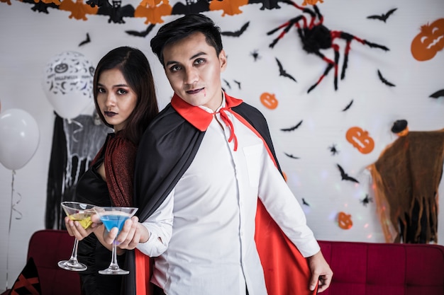 Jong Aziatisch stel in kostuumheks en dracula met Halloween-feest vieren en samen wijn drinken op Halloween-festival in de kamer thuis. Concept paar vieren Halloween samen thuis.