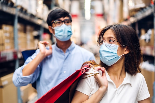Jong aziatisch stel in quarantaine voor coronavirus met chirurgisch masker gezichtsbescherming met sociale afstand en boodschappentas in de winkel. covid19 en nieuw normaal concept