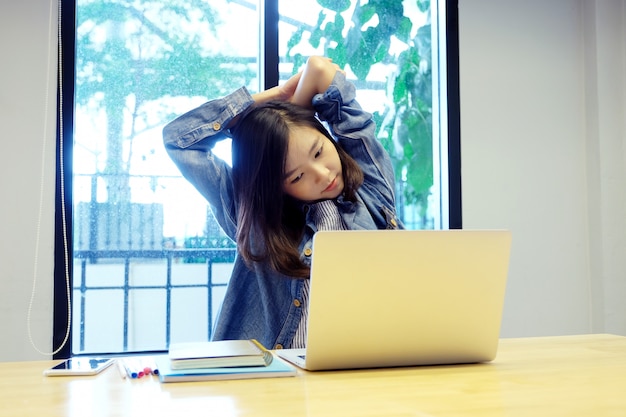 Jong aziatisch vrouwen uitrekkend lichaam om te ontspannen terwijl het werken met laptop computer bij haar bureau