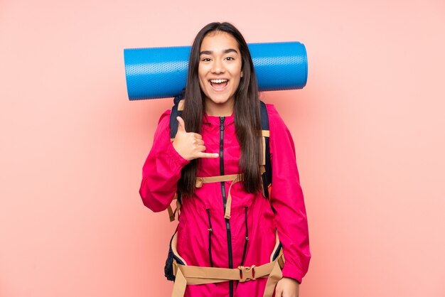 Jong bergbeklimmer Indisch meisje met een grote rugzak op roze muur die telefoongebaar maken