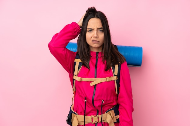 Jong bergbeklimmermeisje met een grote rugzak over geïsoleerde roze muur met een uitdrukking van frustratie en niet begrip