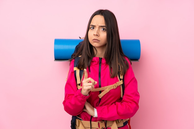 Jong bergbeklimmermeisje met een grote rugzak over roze gefrustreerd en wijzend op de voorkant