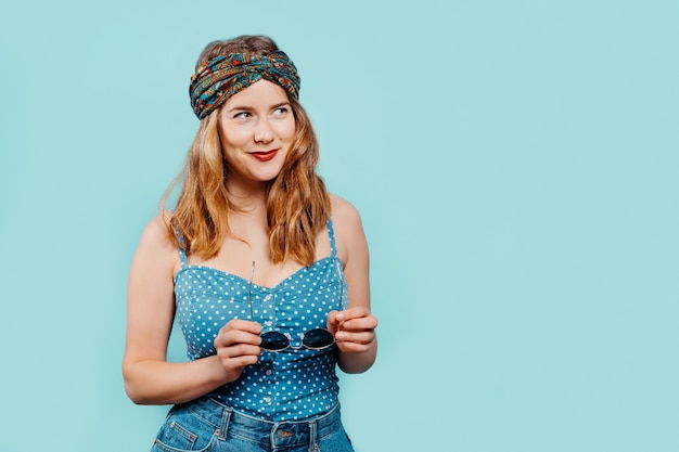 jong blond meisje met een heldere hoofddoek met een zonnebril met een denim top op een blauwe achtergrond