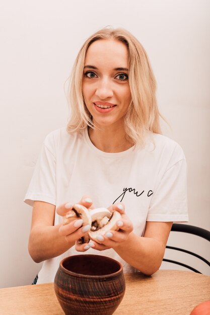 Jong blond meisje met gehakte champignons in haar handen en glimlachend