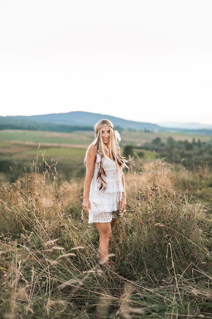 Jong blond mooi hippiemeisje in witte kleding op de zomergebied
