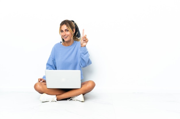 Jong blond Uruguayaans meisje met laptop die op witte muur wordt geïsoleerd die en een vinger als teken van het beste opheft