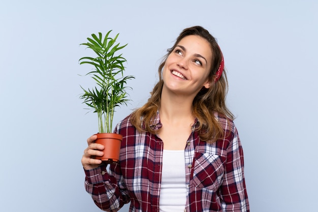 Jong blonde tuinmanmeisje die een installatie houden omhoog kijkend terwijl het glimlachen