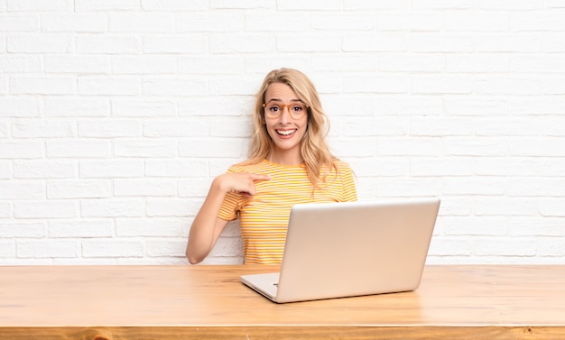 jong blondemeisje bij laptop die gelukkig trots en verrast kijken