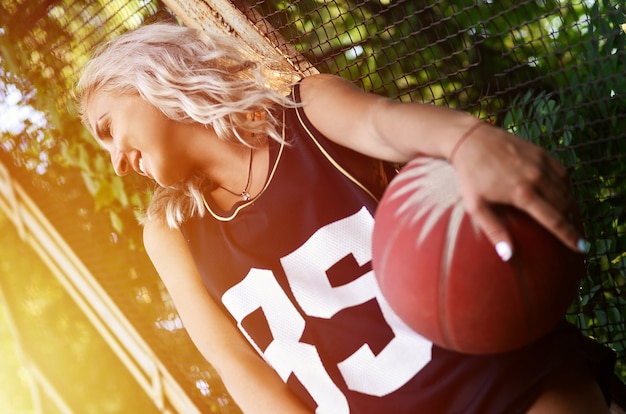 Jong blondemeisje met oranje basketbal die in openlucht stellen