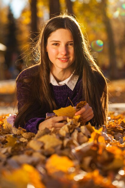 Jong brunette meisje in een paarse trui ligt op gevallen herfstbladeren