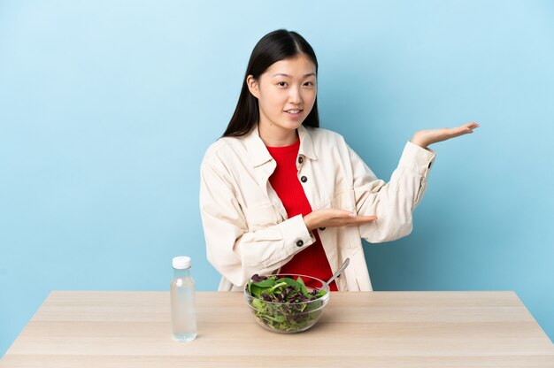 Jong chinees meisje dat een salade eet die handen aan de kant uitbreidt voor het uitnodigen om te komen