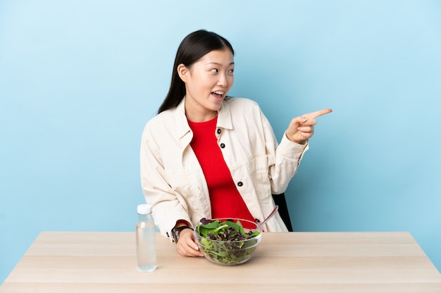 Jong Chinees meisje dat een salade eet die vinger aan de kant richt en een product voorstelt