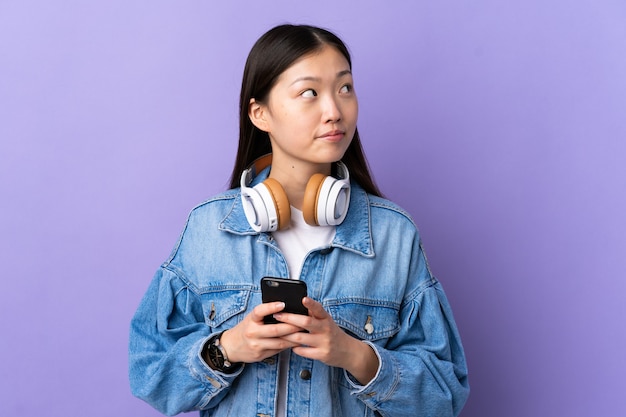 Jong Chinees meisje over geïsoleerde paarse het luisteren muziek met gsm en denken