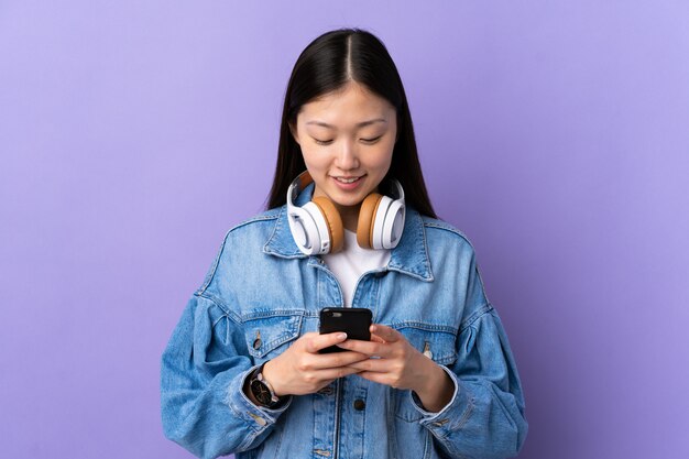 Jong Chinees meisje over geïsoleerde paarse luisteren muziek en op zoek naar mobiel
