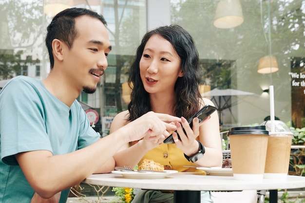 Jong chinees stel bespreekt berichten of foto's op sociale media terwijl ze genieten van een romantische date op het terras